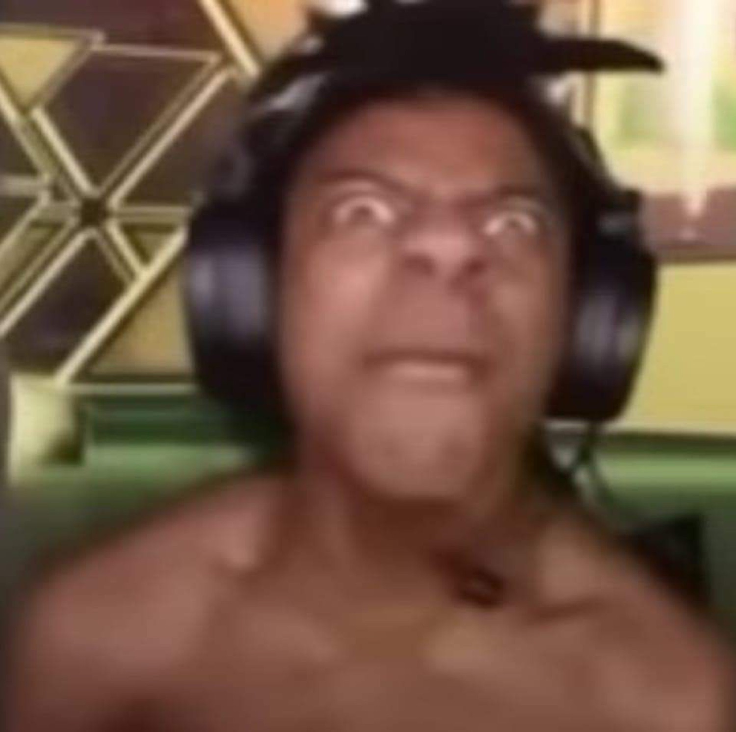 Blurry shirtless man in headphones scowling intensely into his webcam