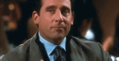 Steve Carell in a suit winking and pointing with a drink