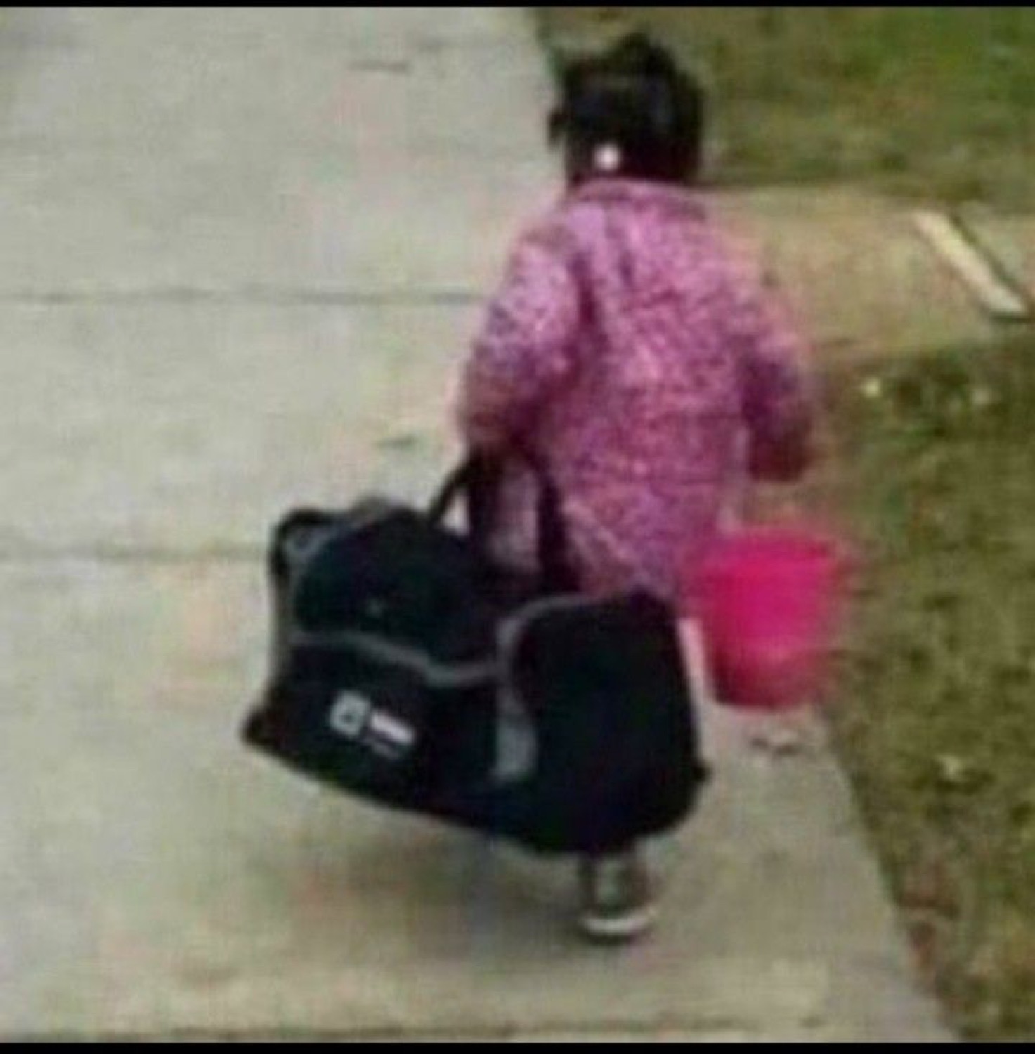 Little kid seen from behind lugging a big duffel bag and a pink bucket