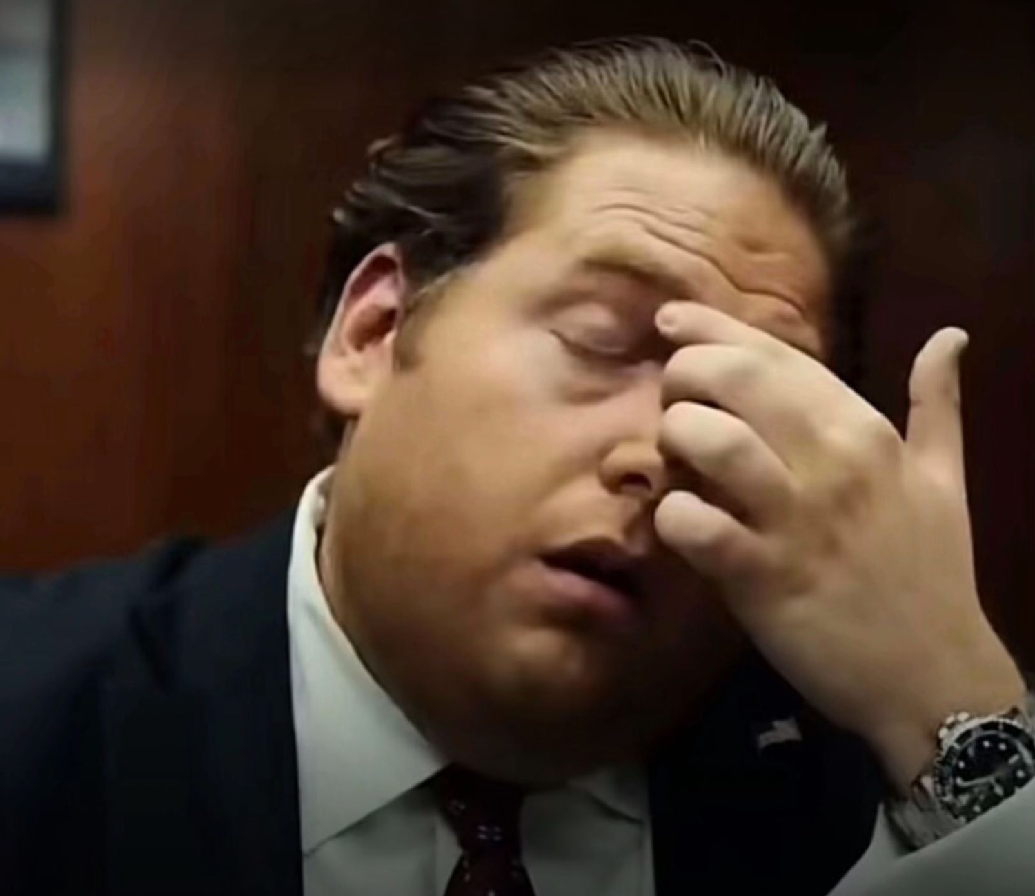 Jonah Hill in a suit doing a full facepalm with eyes closed and mouth open