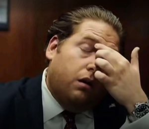 Jonah Hill in a suit doing a full facepalm with eyes closed and mouth open