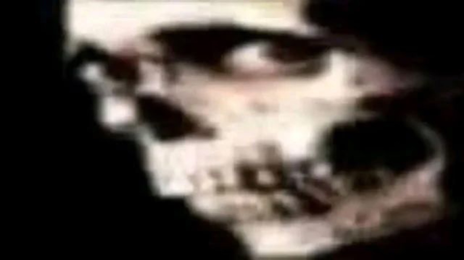 Grainy, dark, heavily blurred close-up of a shadowy skull-like face
