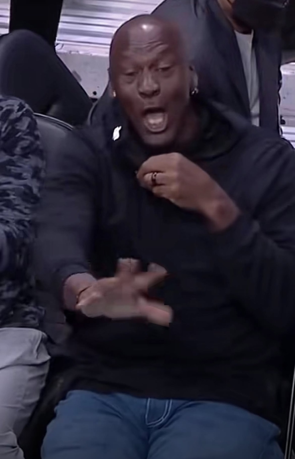 Michael Jordan in a black hoodie laughing and gesturing courtside