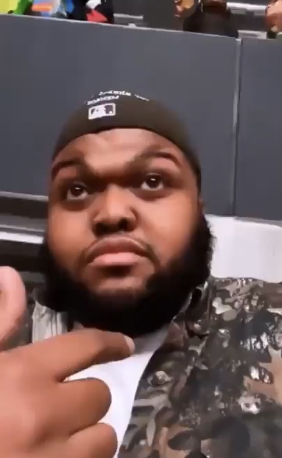 Man in a backwards cap pointing at himself
