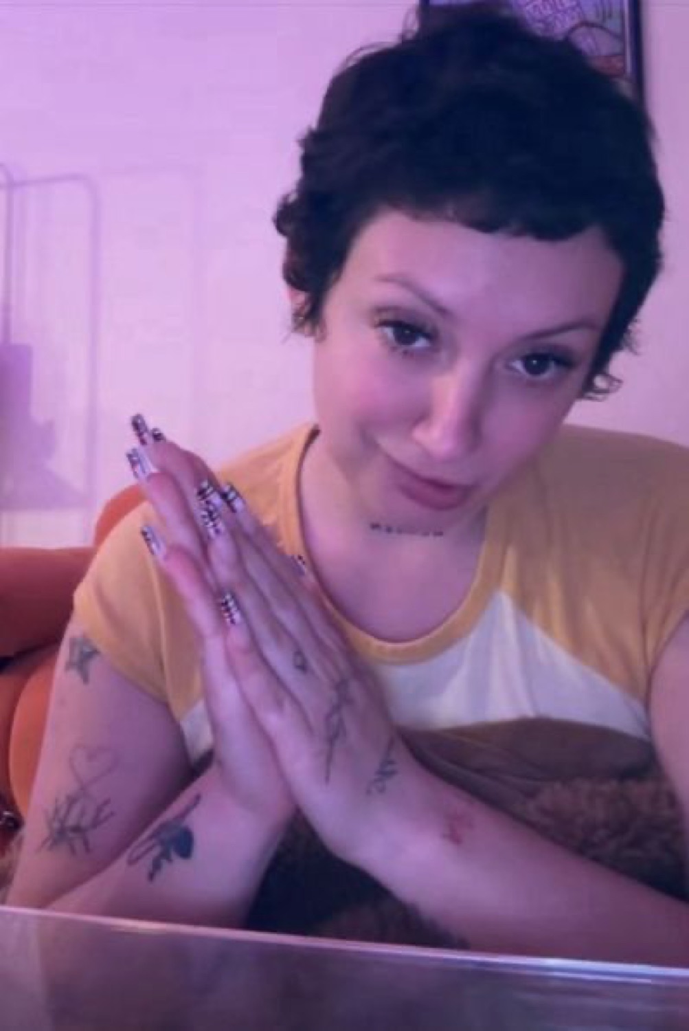 Tattooed woman pressing hands together with a sly smile, looking straight at camera