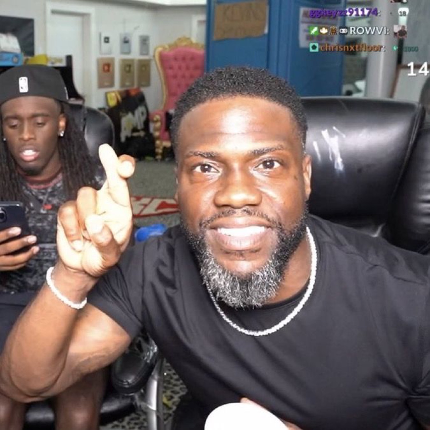 Kevin Hart on a livestream holding up a finger mid-point, grinning like he's got a point
