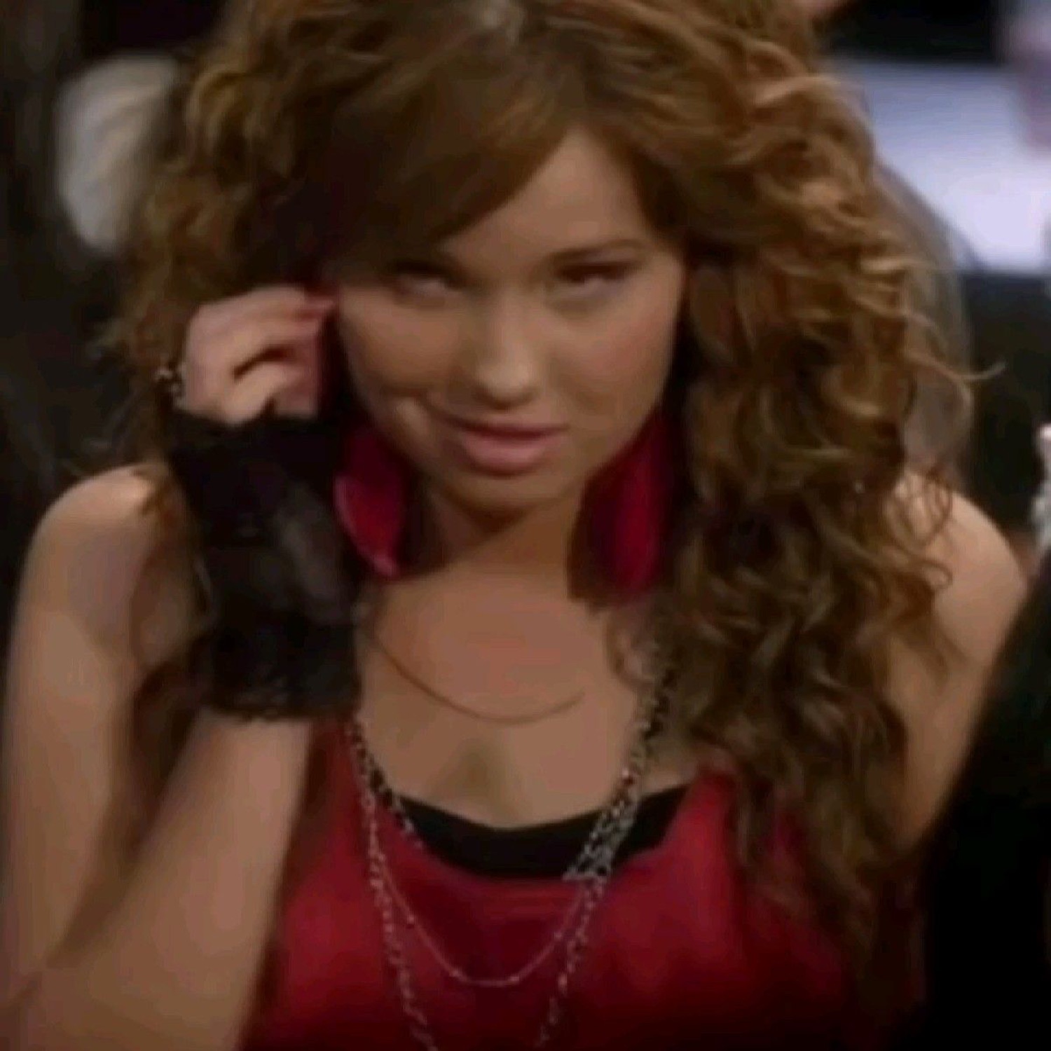 Curly-haired girl in a red top smirking smugly to the side