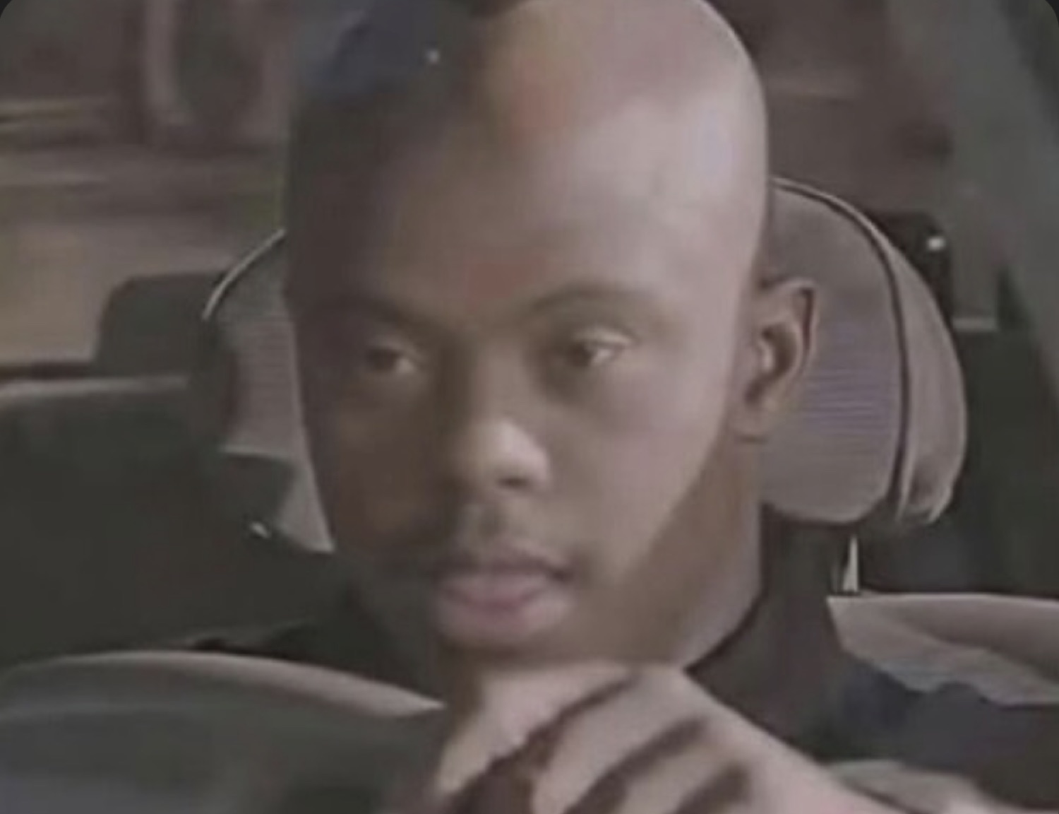 Bald man in a car turning to stare at the camera