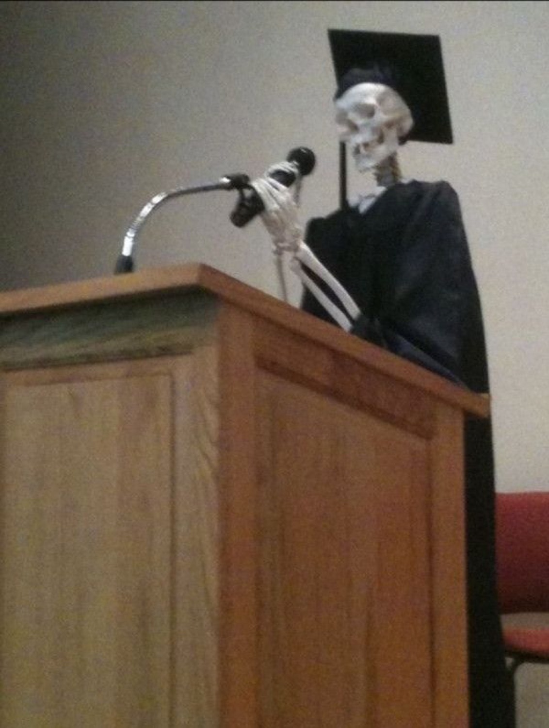 Skeleton in a graduation cap giving a speech at a podium