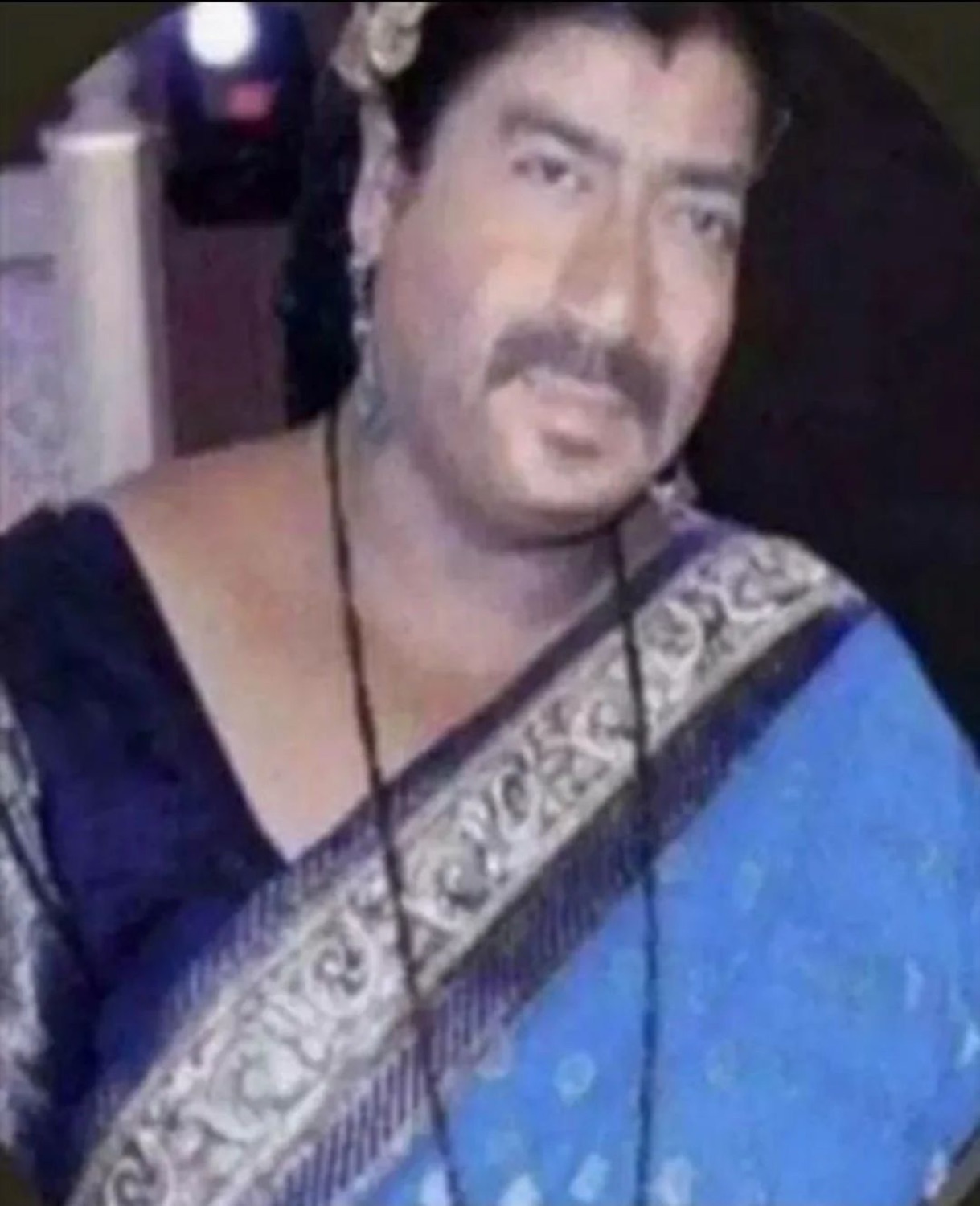 Mustached man in a sari and wig staring with a serious face