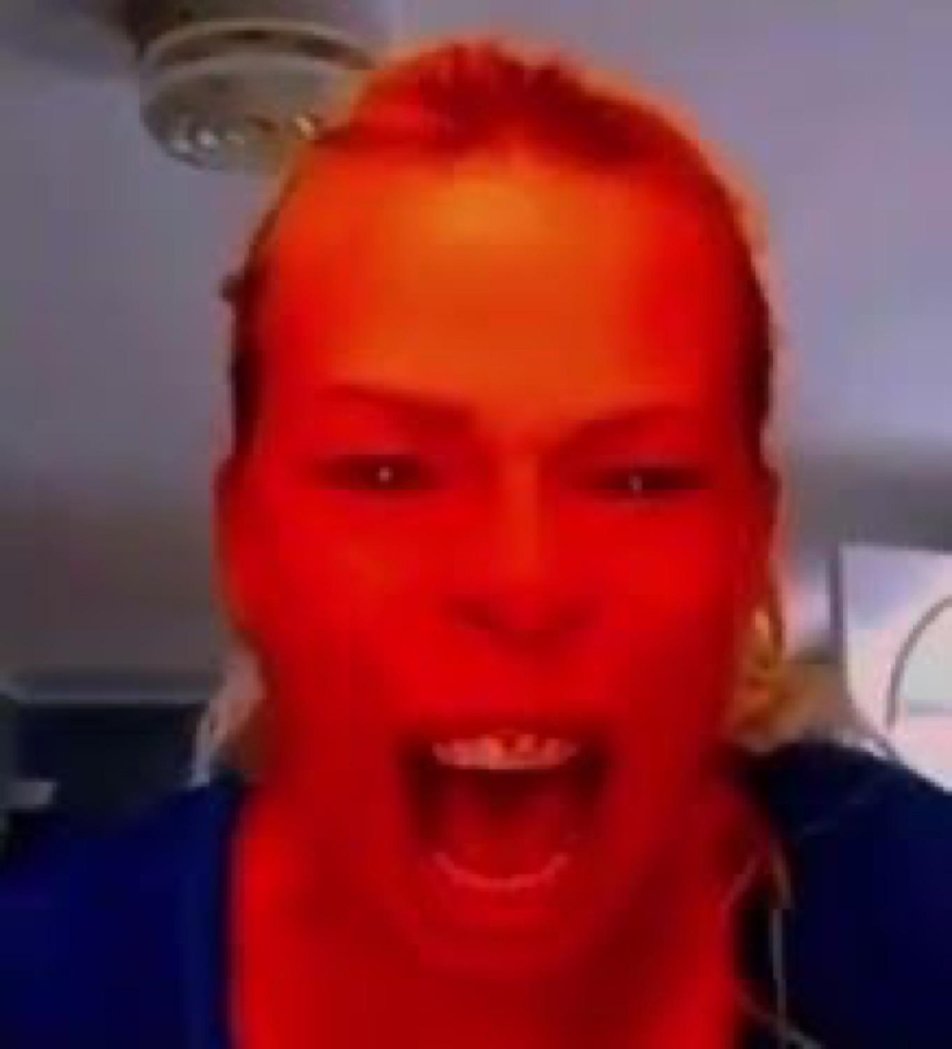 Red-tinted close-up of a woman screaming wide-mouthed at the camera