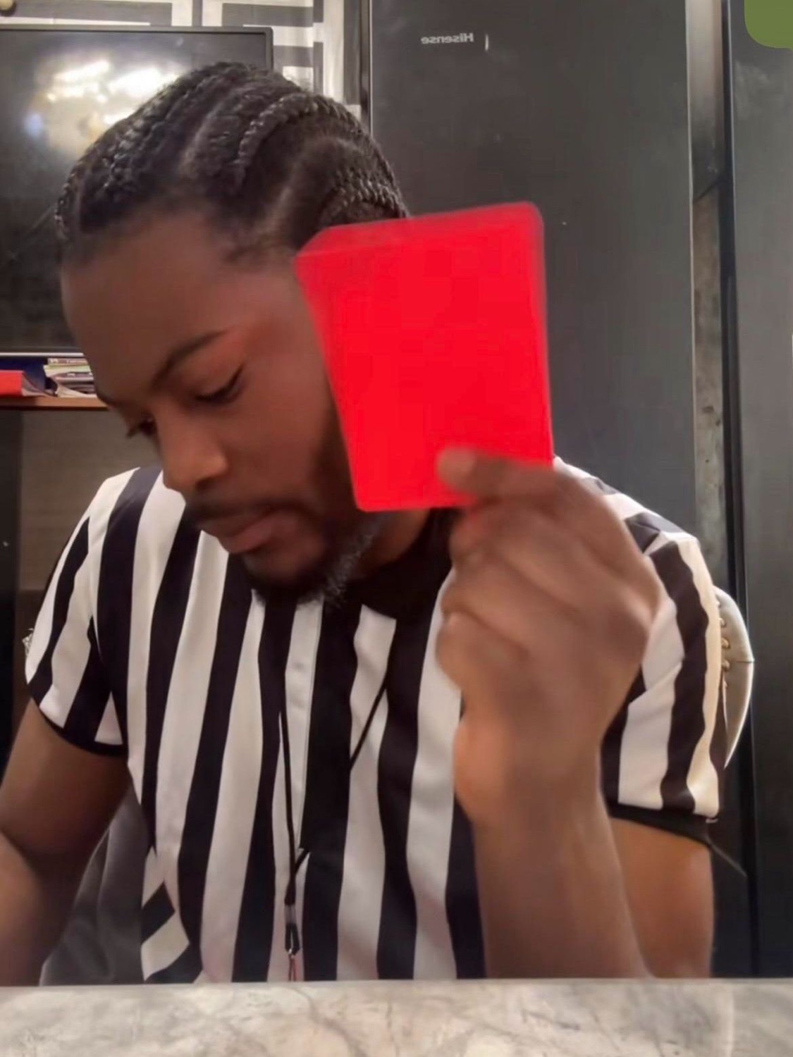 Referee in a striped jersey holding up a red card with a done, unimpressed look