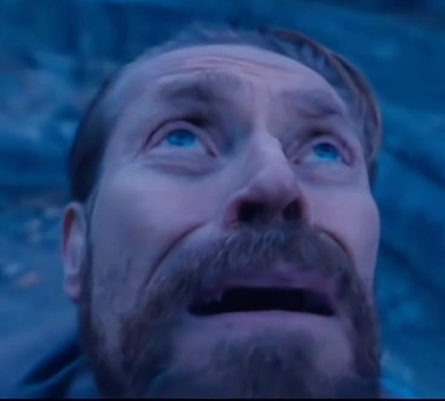 Bearded man lying on the ground gazing up with a terrified, tearful stare