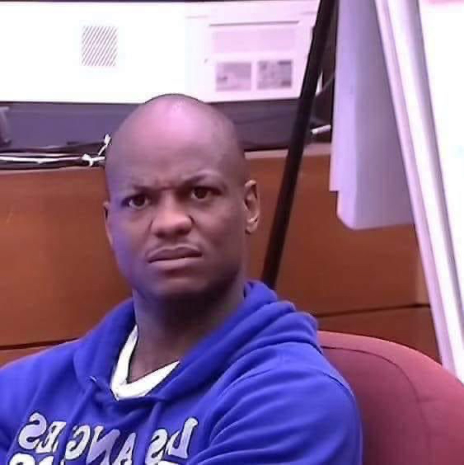 Man in a blue hoodie shooting a skeptical, side-eyeing frown at an office desk