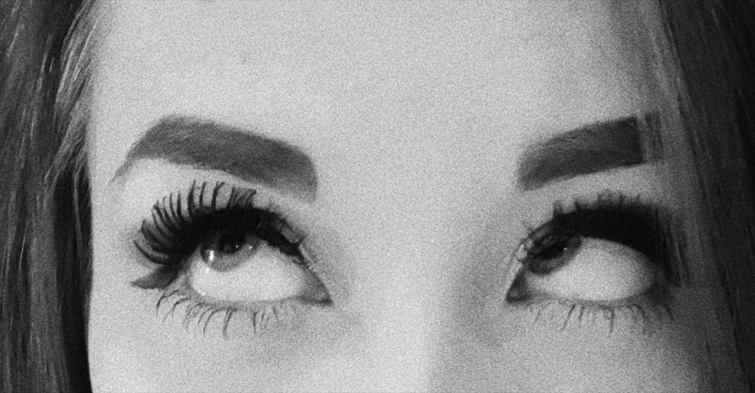 Close-up black-and-white shot of a woman's eyes with dramatic lashes giving a sharp sideways glare