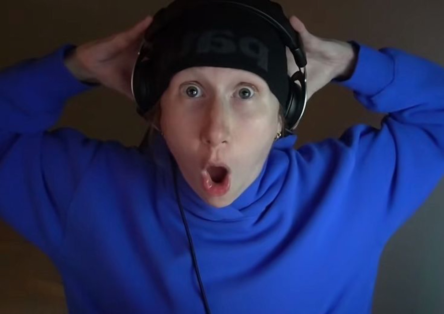 Person in a blue hoodie and headset grabbing their head, mouth open in total shock