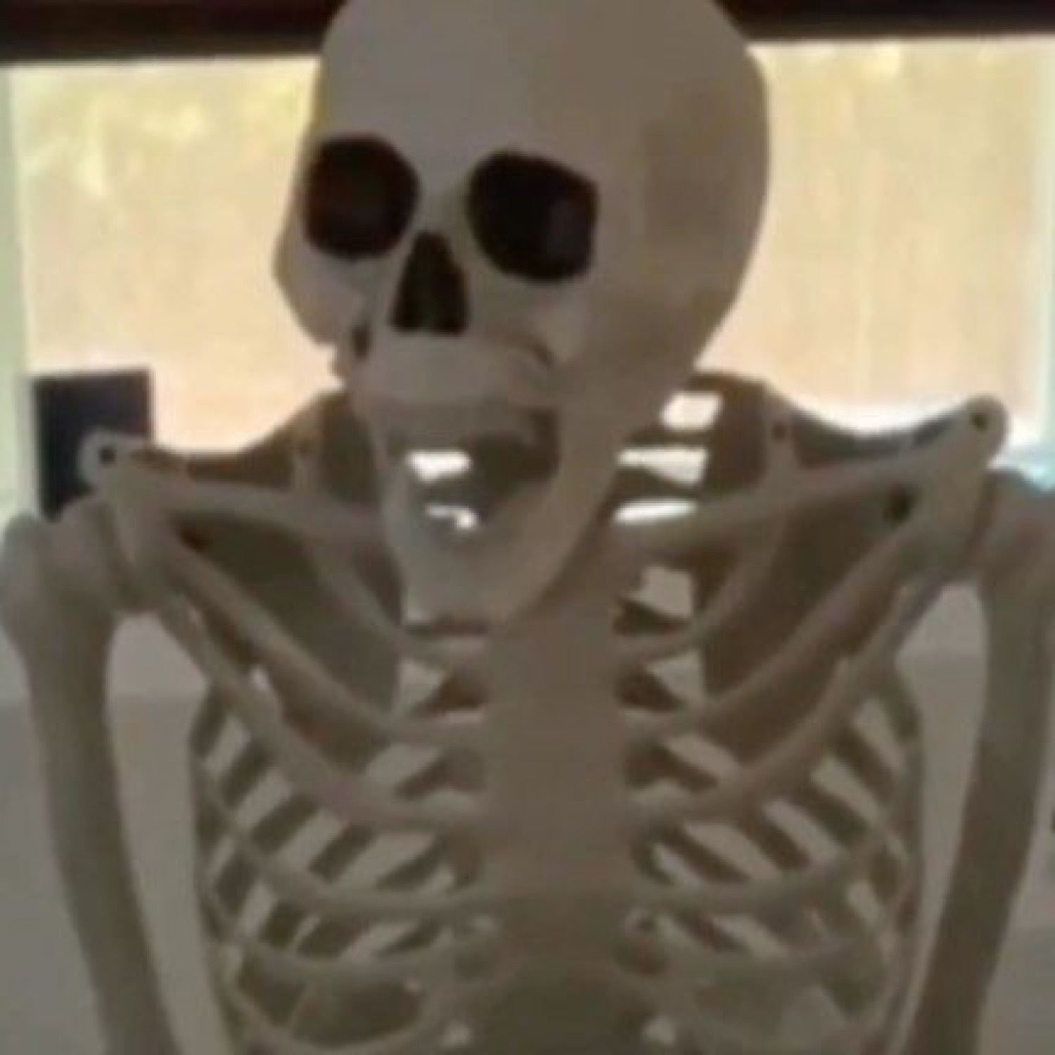 Plastic Halloween skeleton hunched at a table staring at its phone with dead-eyed dedication