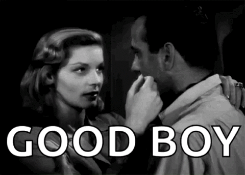 Black and white film of a woman leaning in to a man, "Good boy"