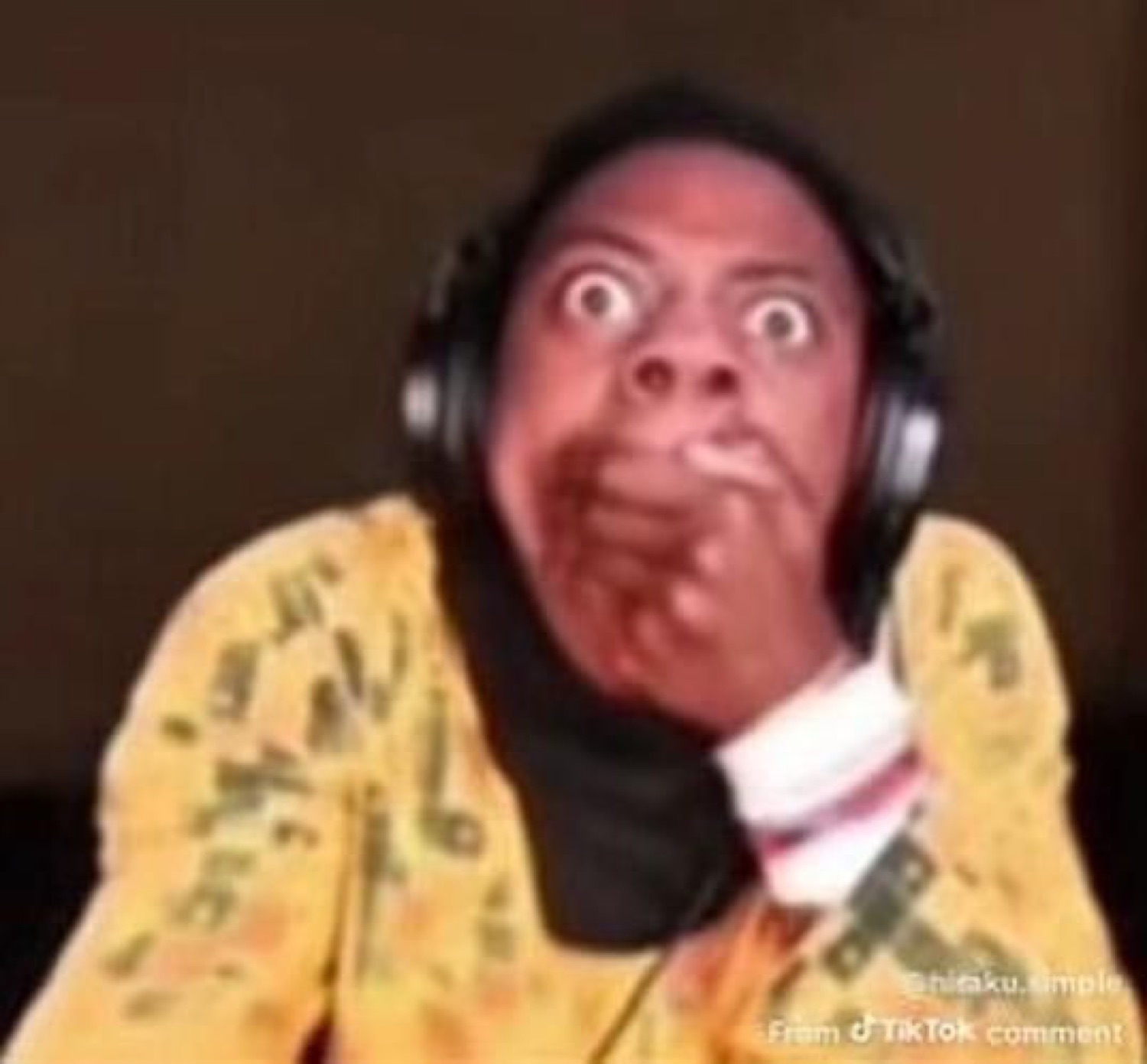 Person in headphones with bulging eyes covering their mouth in shock