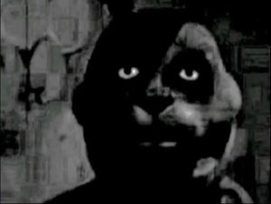 Dark grainy black-and-white face staring with glowing eyes into the camera