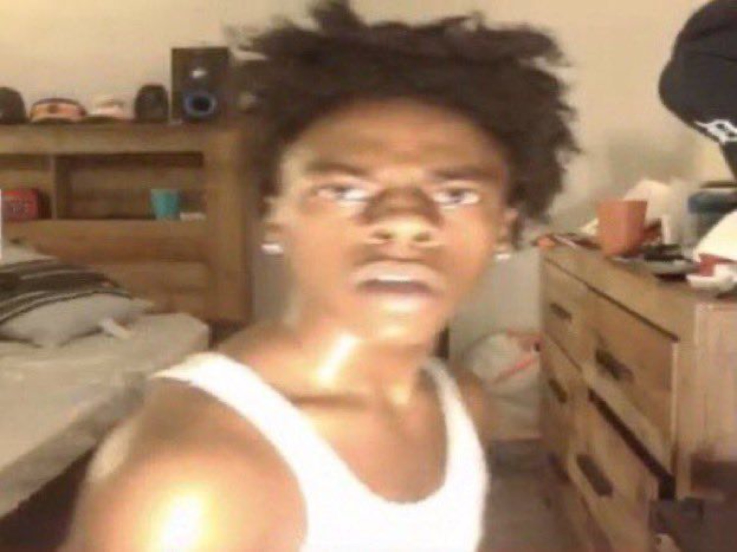 Guy in a white tank top leaning into the camera with a totally blank, glazed stare