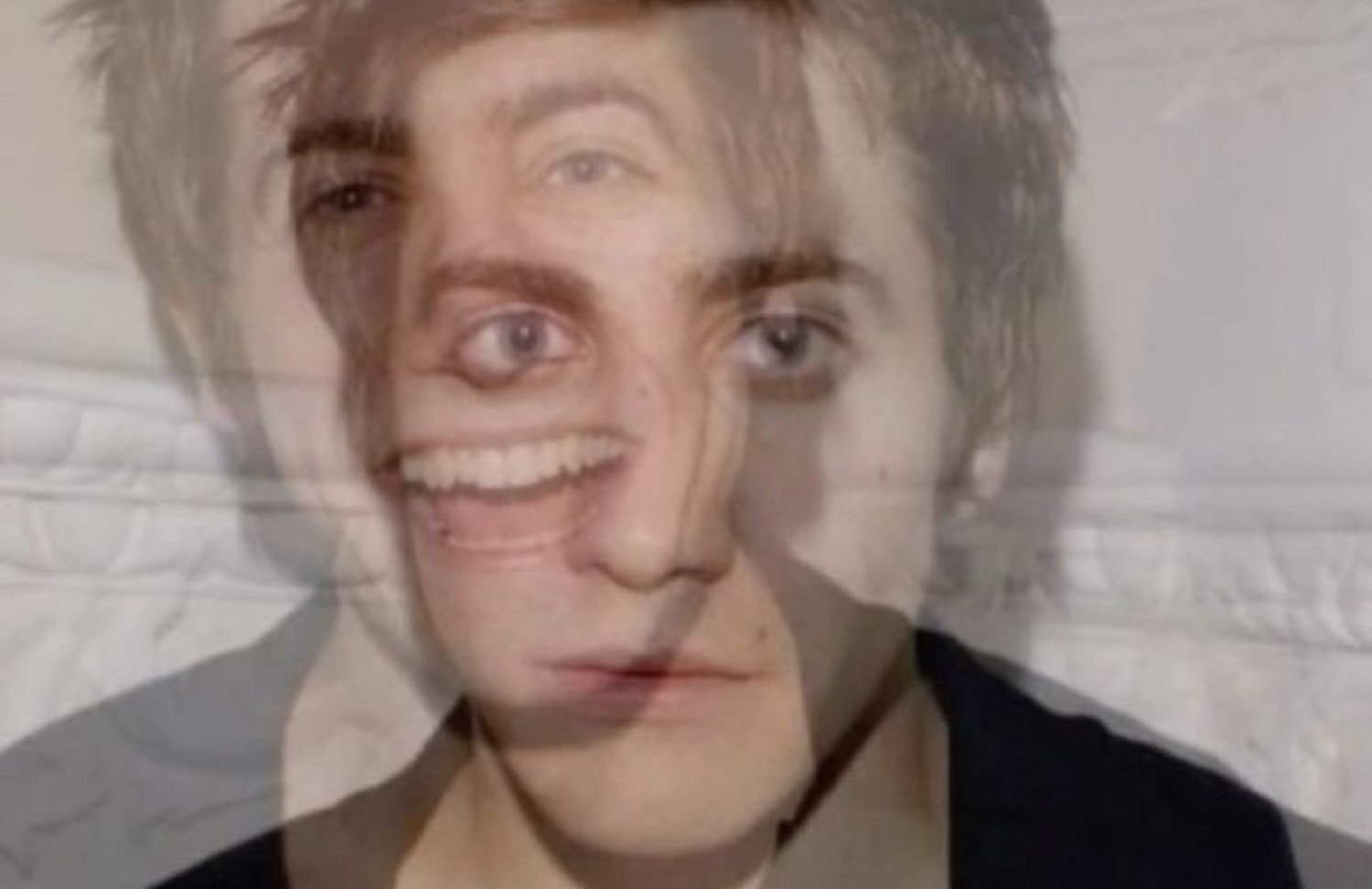 Person with a forced manic grin staring intensely into the camera, face double-exposed