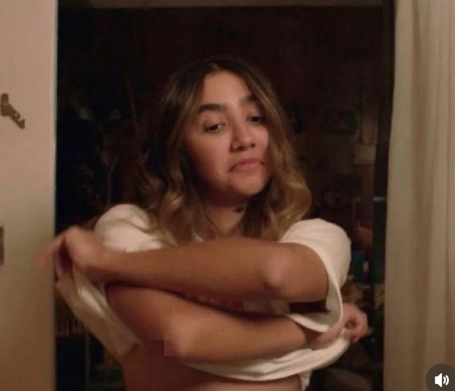 Girl in a doorway pulling at her top with a smug, self-satisfied smirk
