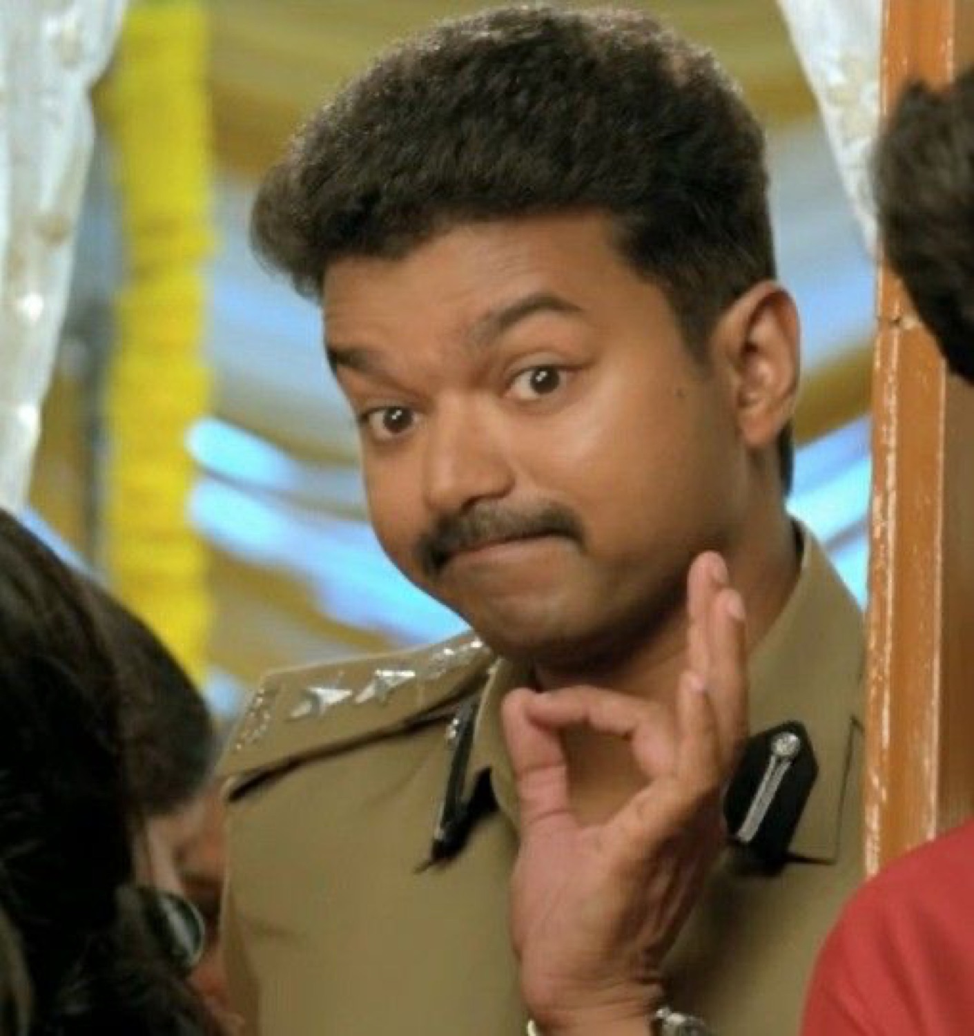 Vijay in police uniform with a smug hand-on-chin look