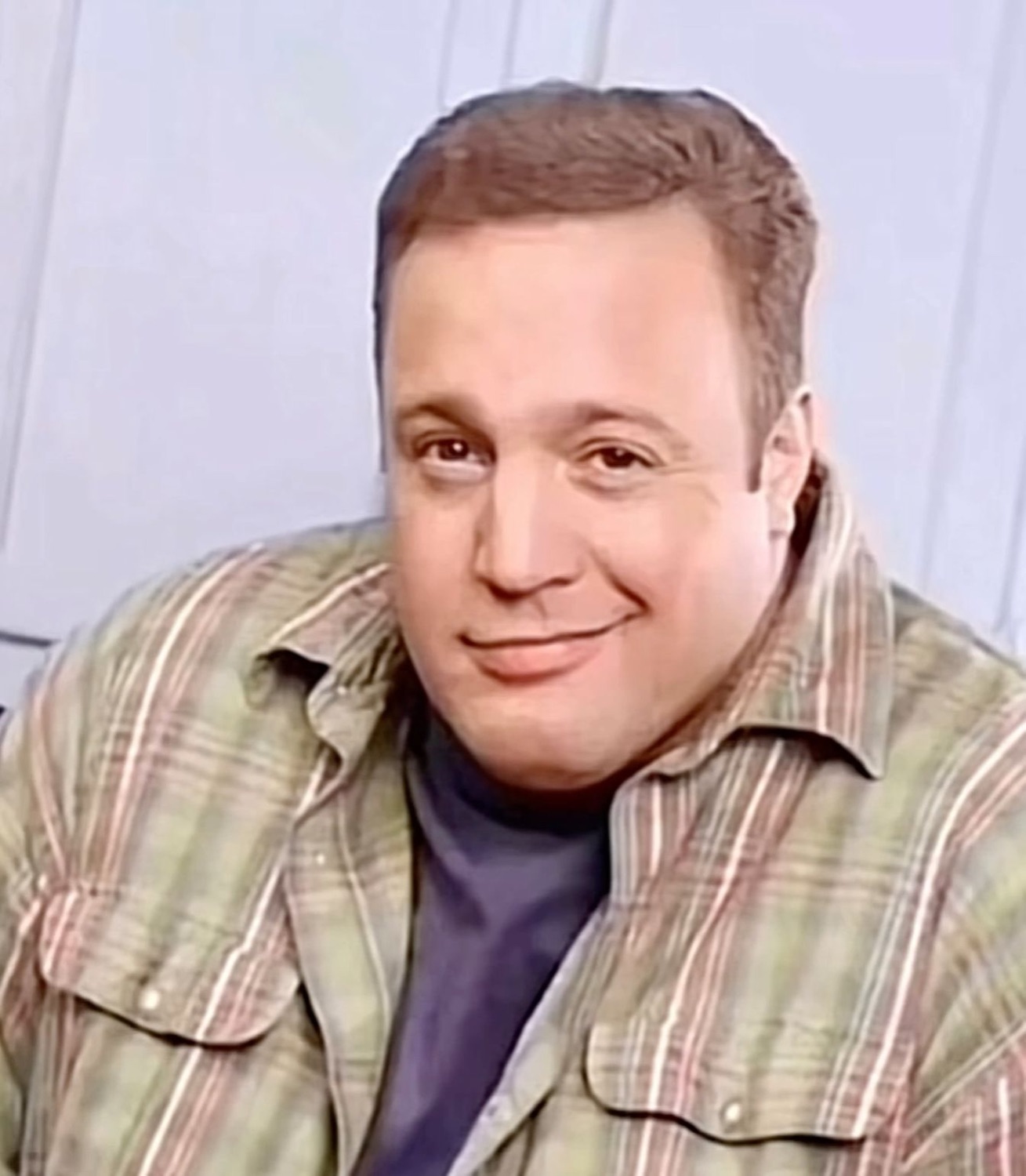 Kevin James leaning with a sly, self-satisfied smirk in a plaid shirt