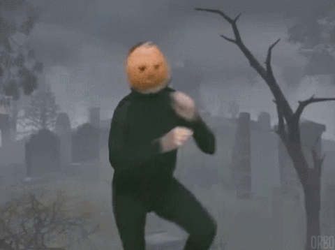 Man with a pumpkin on his head dancing in a cemetery