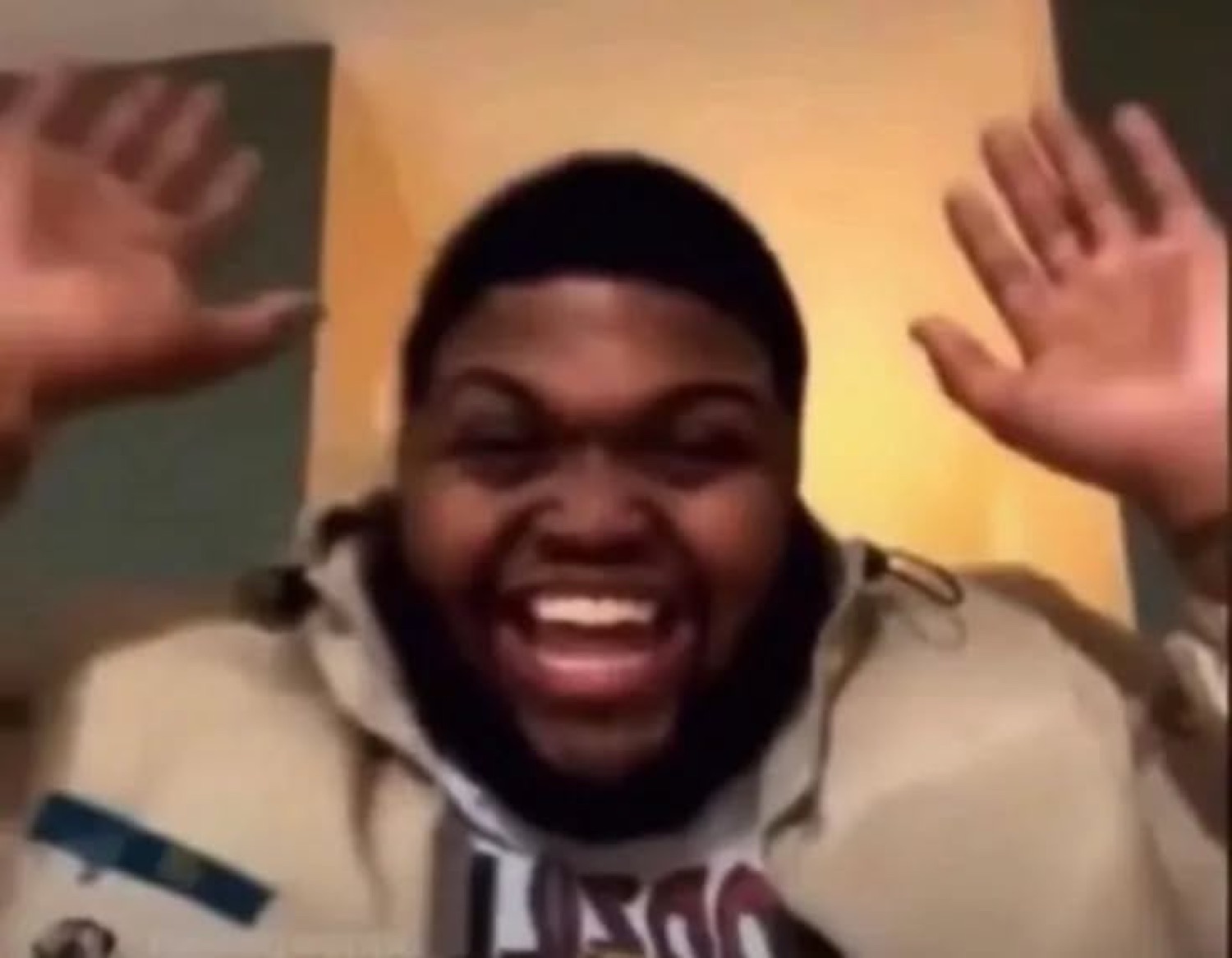 Man in a tan hoodie throwing his hands up and screaming with excitement at the camera