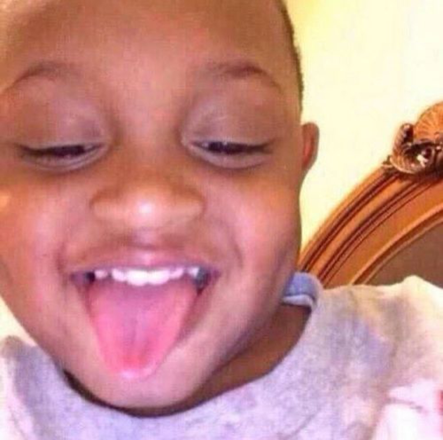 Toddler with squinty eyes and wide grin sticking tongue way out in silly delight