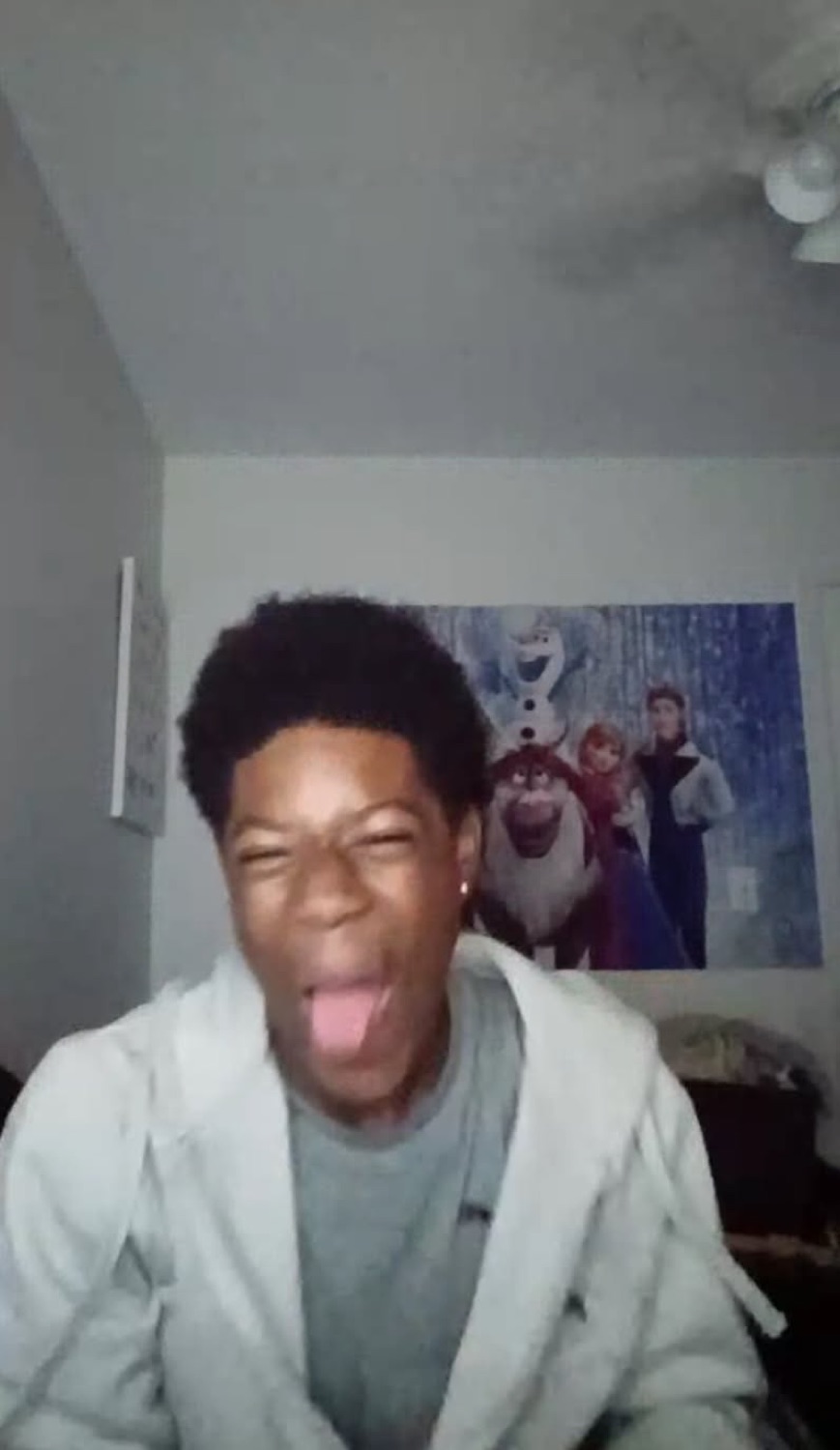 Teen goofing off with tongue out and eyes squeezed shut in front of a Frozen movie poster