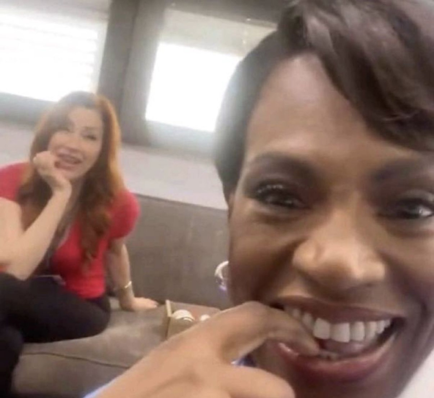 Two women cracking up together, one laughing in the foreground, one smiling behind