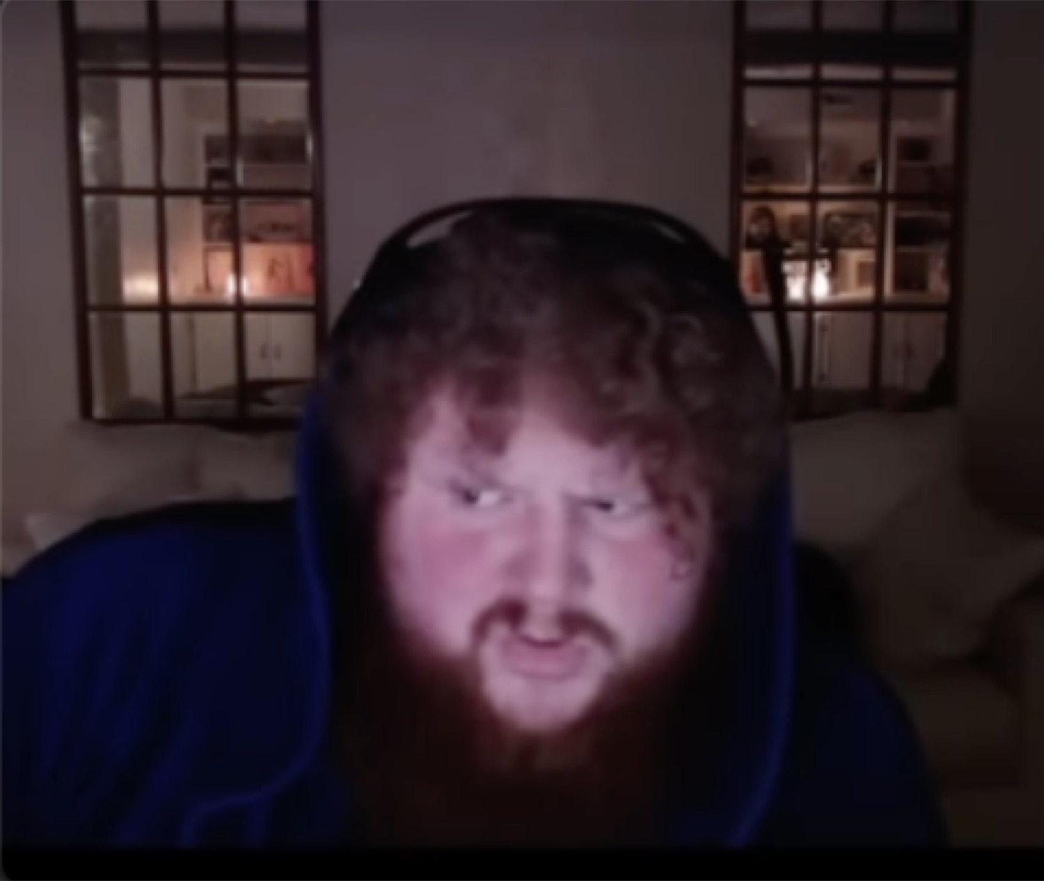 Bearded man in a hoodie leaning into a webcam with a menacing snarl