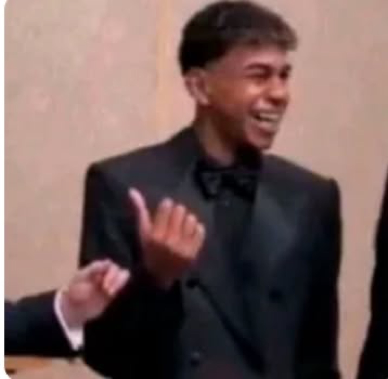 Young man in a tux laughing and waving dismissively