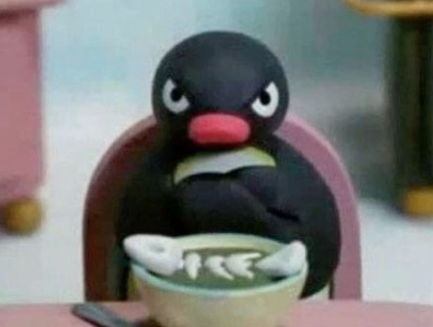 Pingu the penguin hunched over a bowl of fish soup looking intensely angry and unapproachable