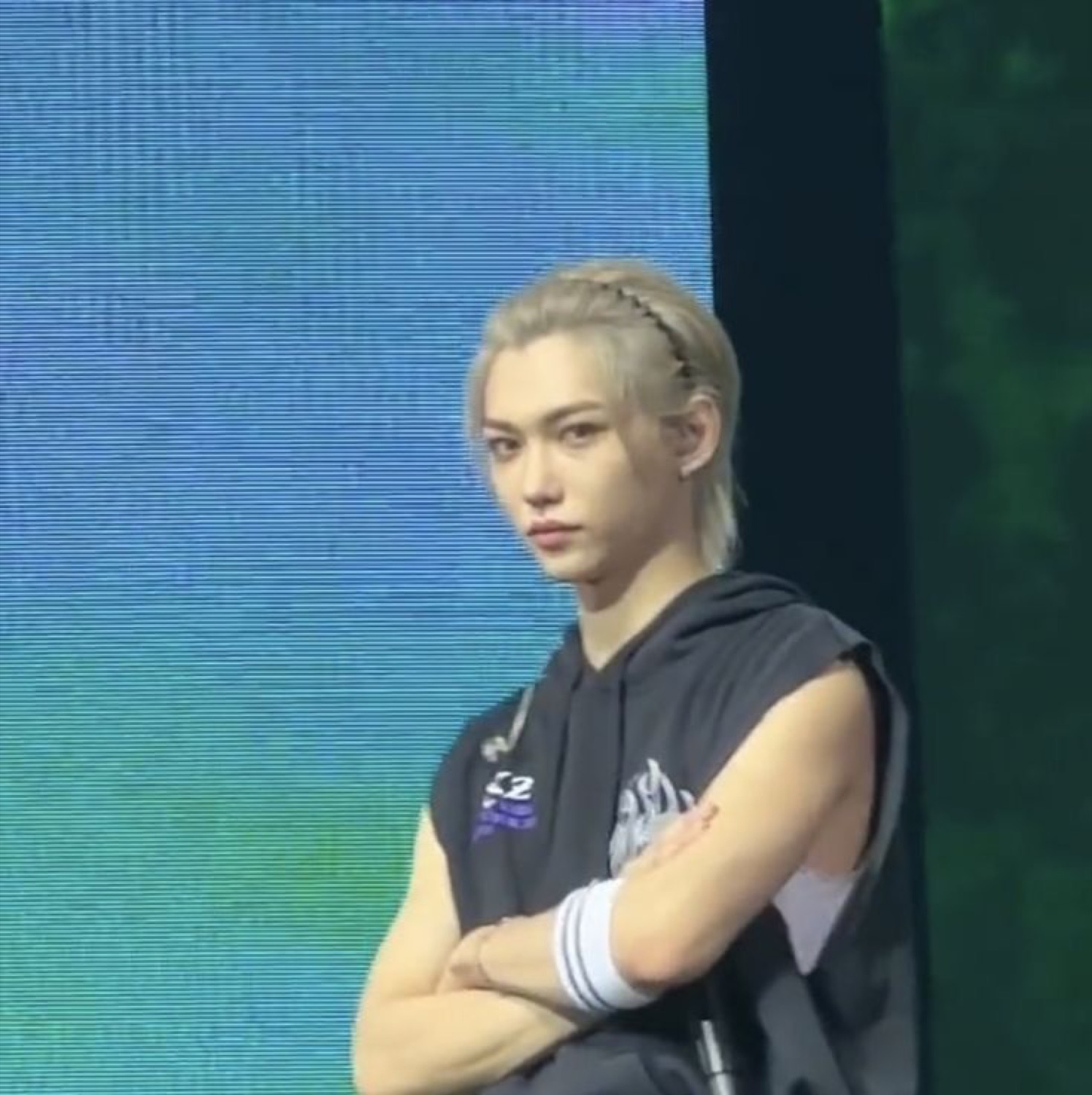 Blond performer on stage with arms crossed and a flat, unimpressed stare