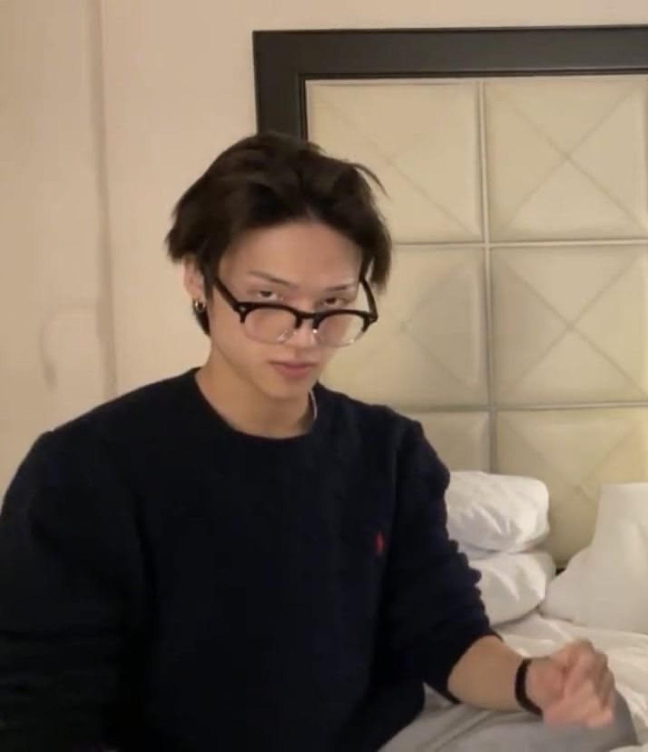 Guy in glasses on a bed giving a flat, judgy stare over the frames