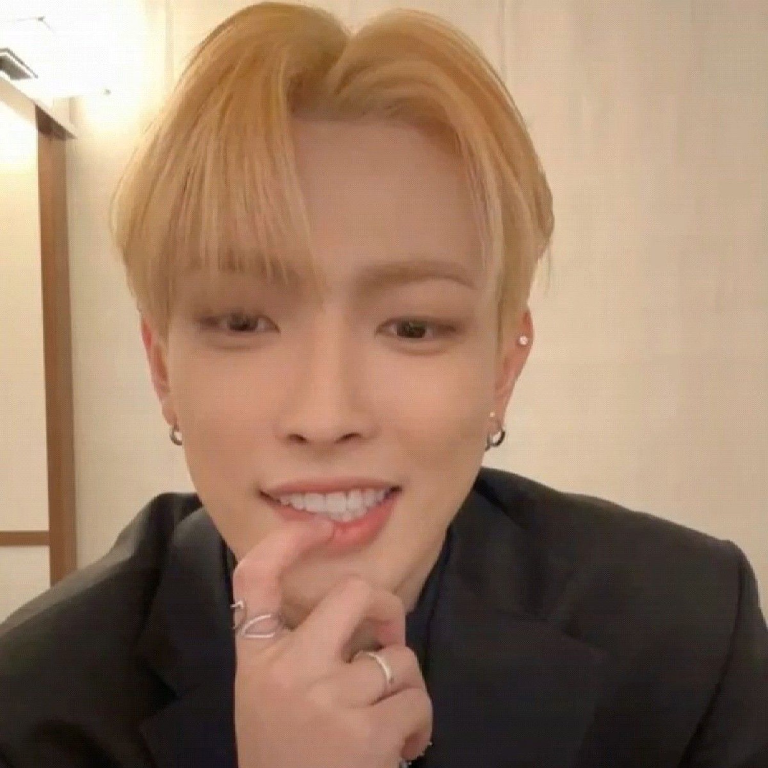 Blond idol in a black blazer biting back a bashful grin with a finger at his lip