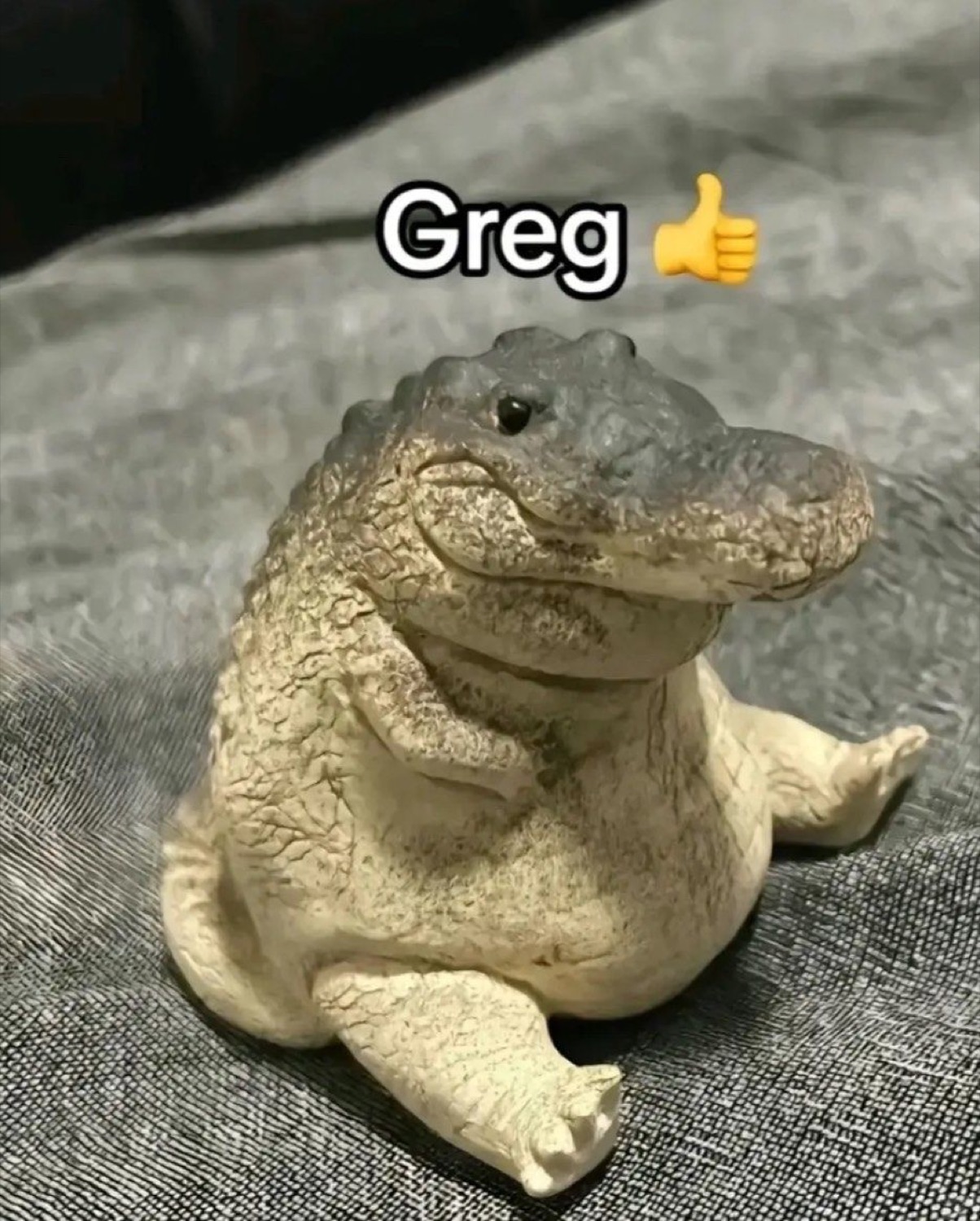 Chubby alligator figurine sitting up with the caption 'Greg' and a thumbs-up emoji