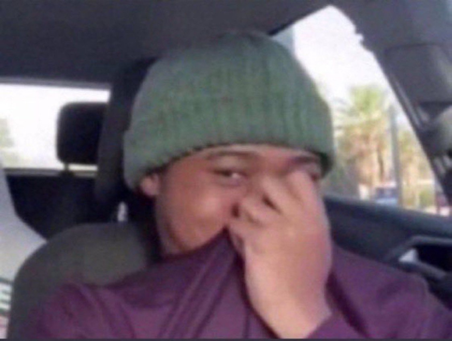 Person in a beanie in a car covering their nose, disgusted