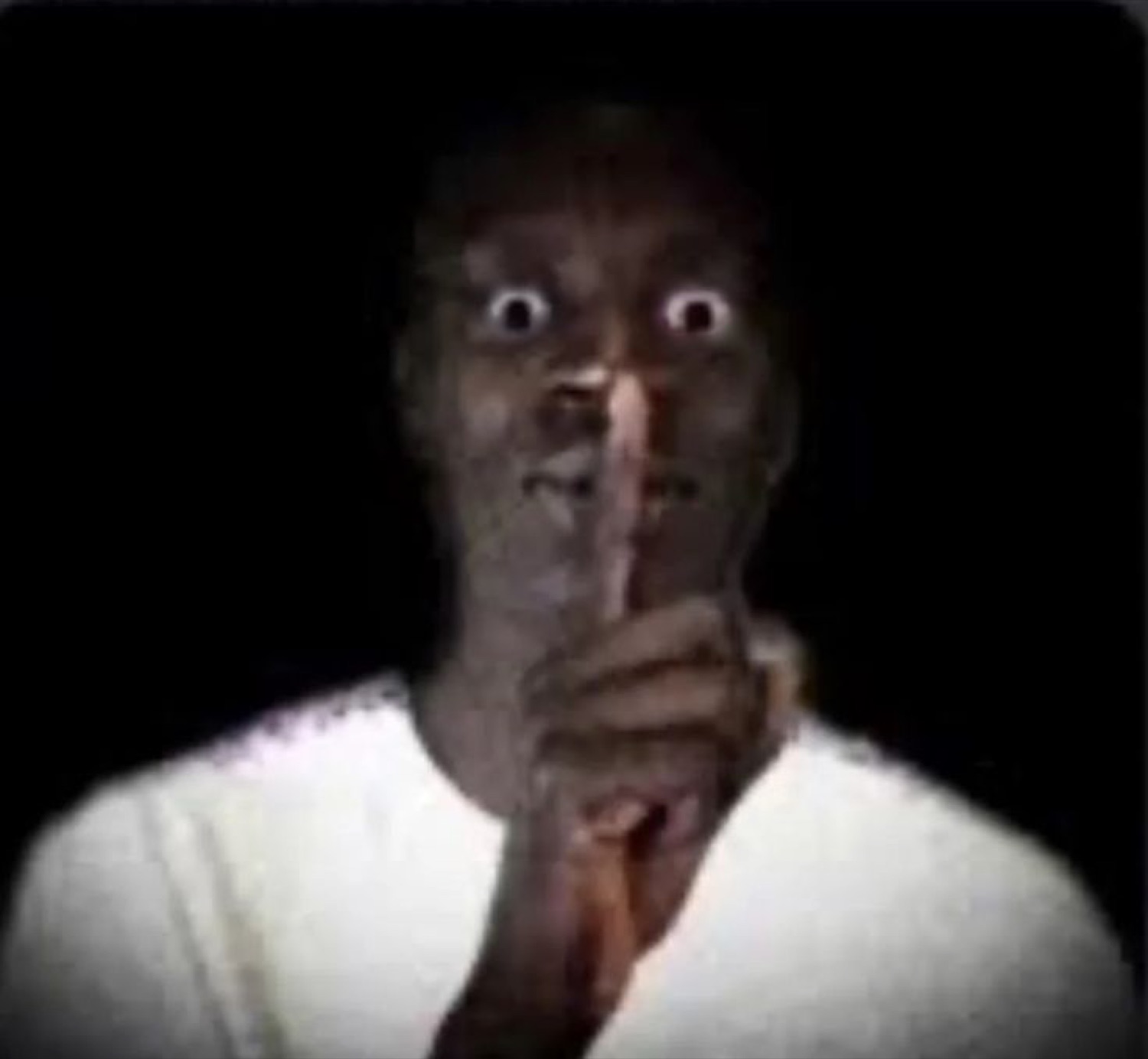 Wide-eyed man in the dark holding a finger to his lips to shush you