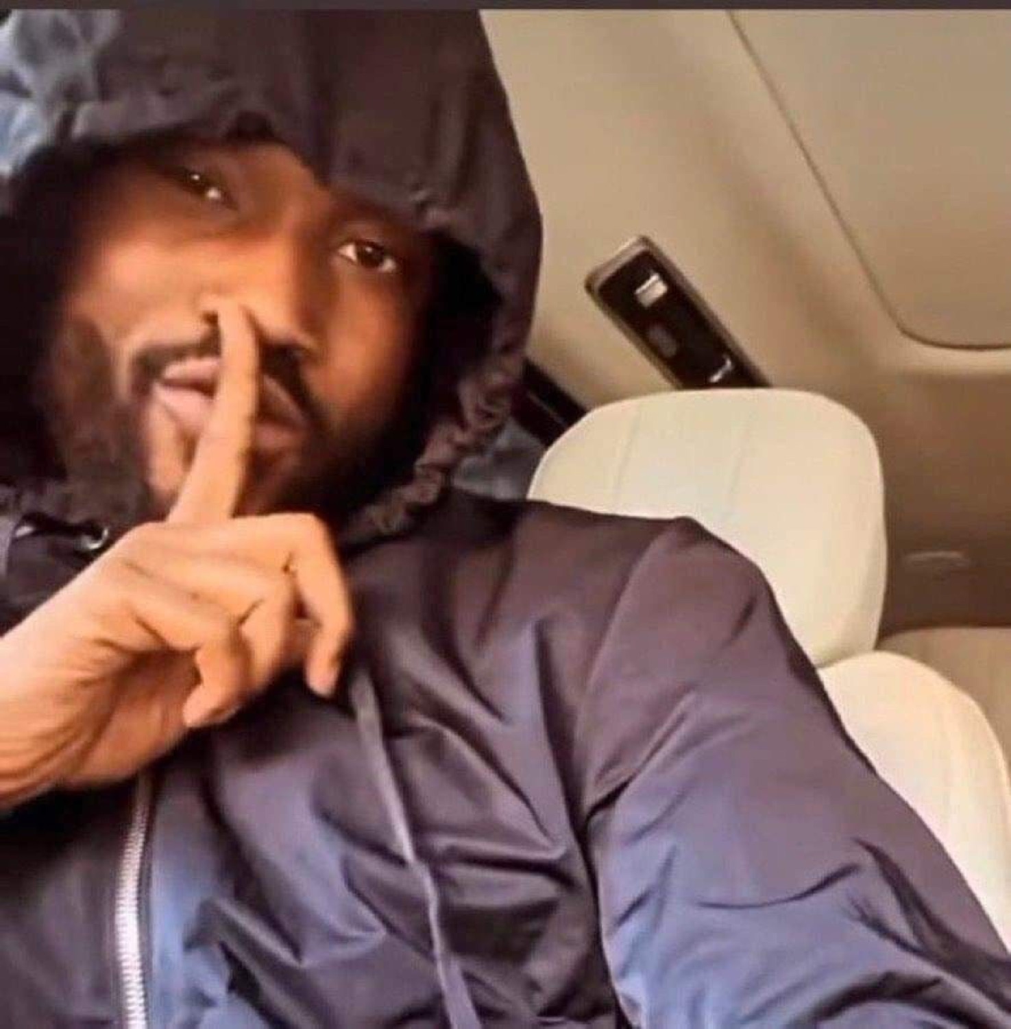 Man in a hood shushing with a finger to his lips