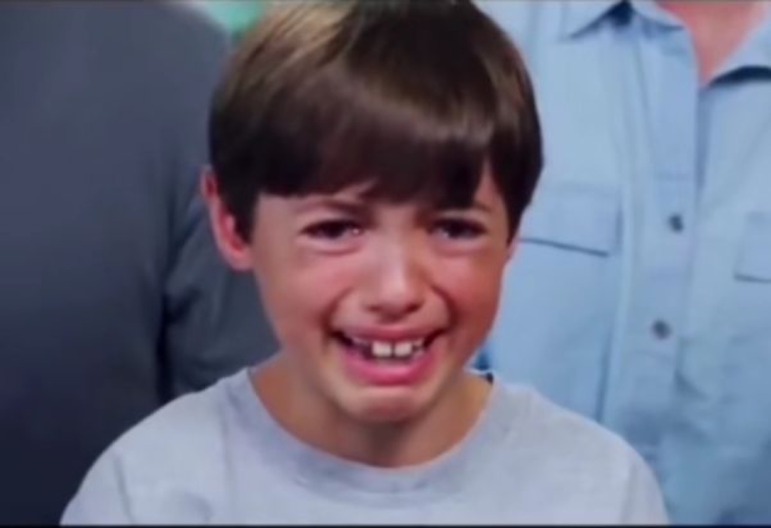 Young boy in a gray shirt breaking into tears with a crumpled, sobbing face