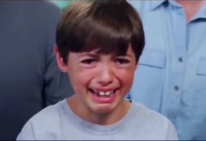 Young boy in a gray shirt breaking into tears with a crumpled, sobbing face