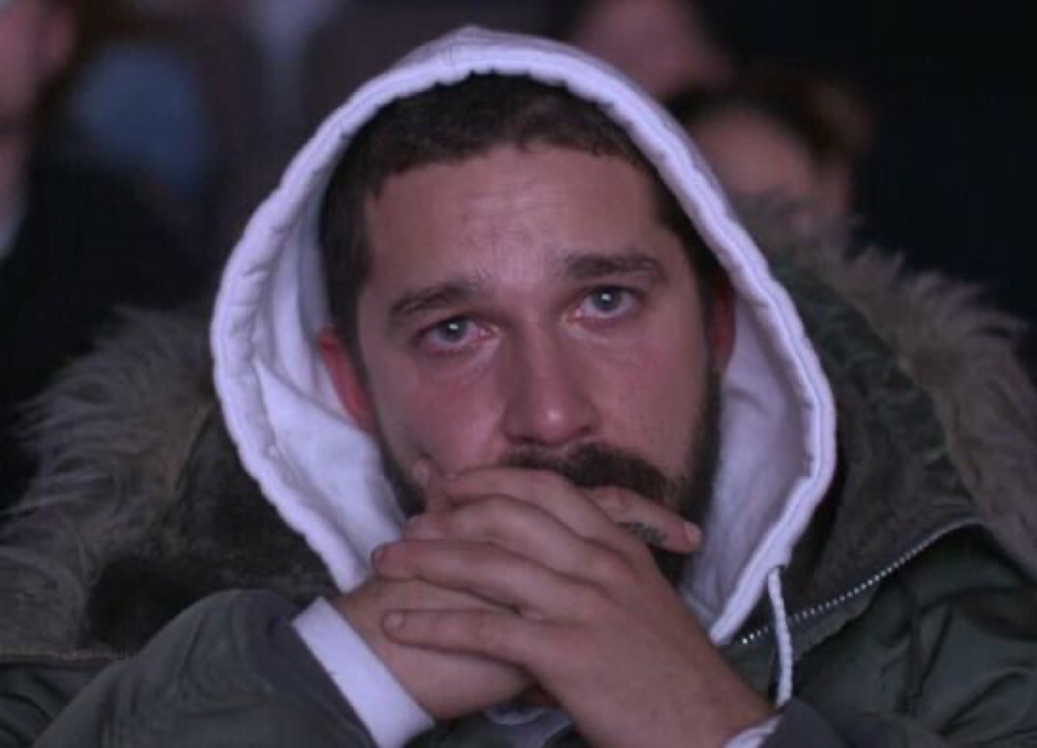 Hooded man in a parka fighting back tears with hands clasped over his mouth