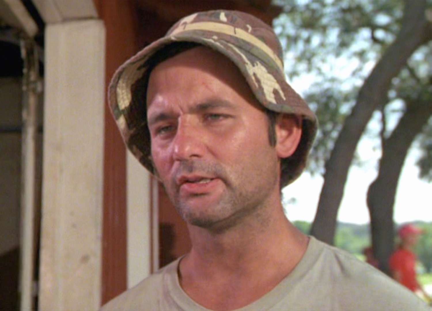 Bill Murray in a bucket hat squinting with dry skepticism at something off-camera