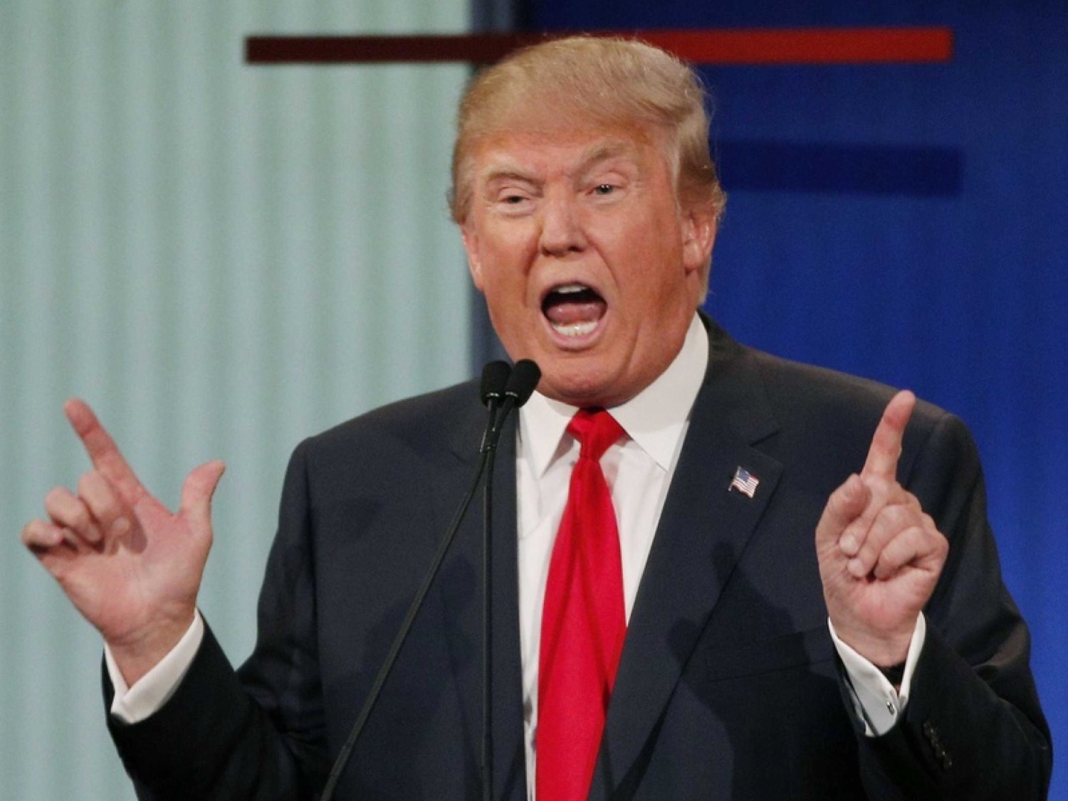 Donald Trump at a podium yelling with both hands raised in his signature emphatic gesture