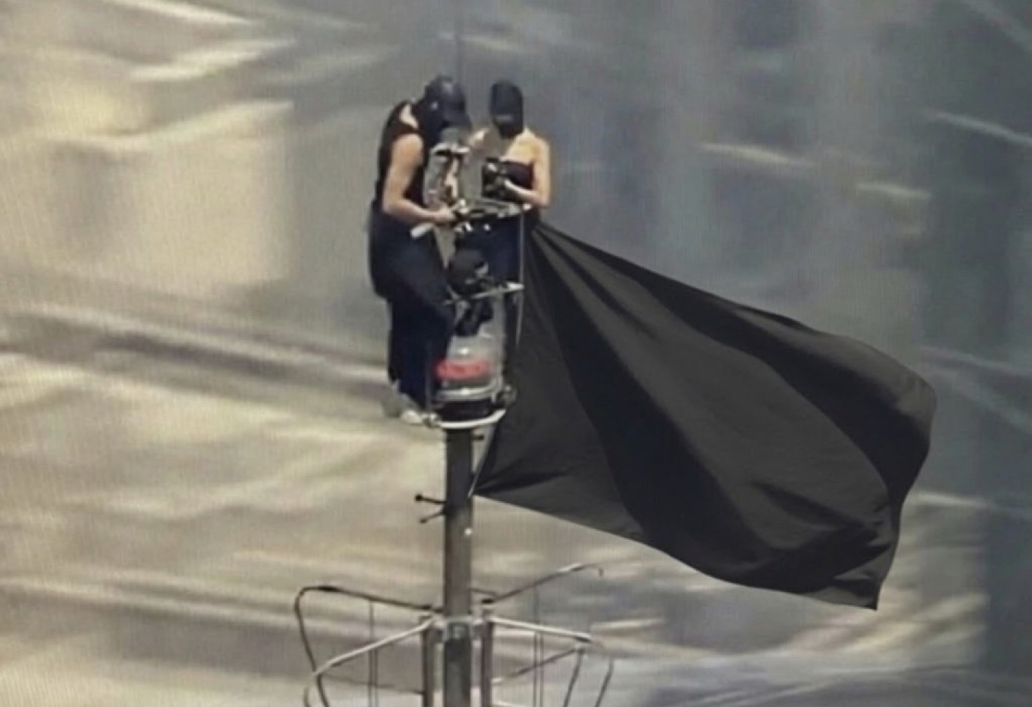 Two masked figures atop a pole raising a huge billowing black flag